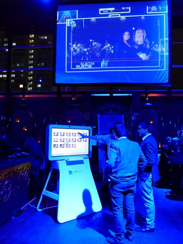 Three men playing with the TapSnap photo booth. Above them is a projection screen displaying an event photo through SnapCast